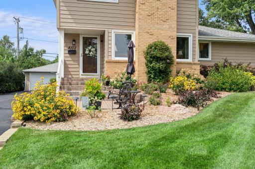 The front paver patio offers a charming spot to relax, framed by vibrant, professionally landscaped garden beds.