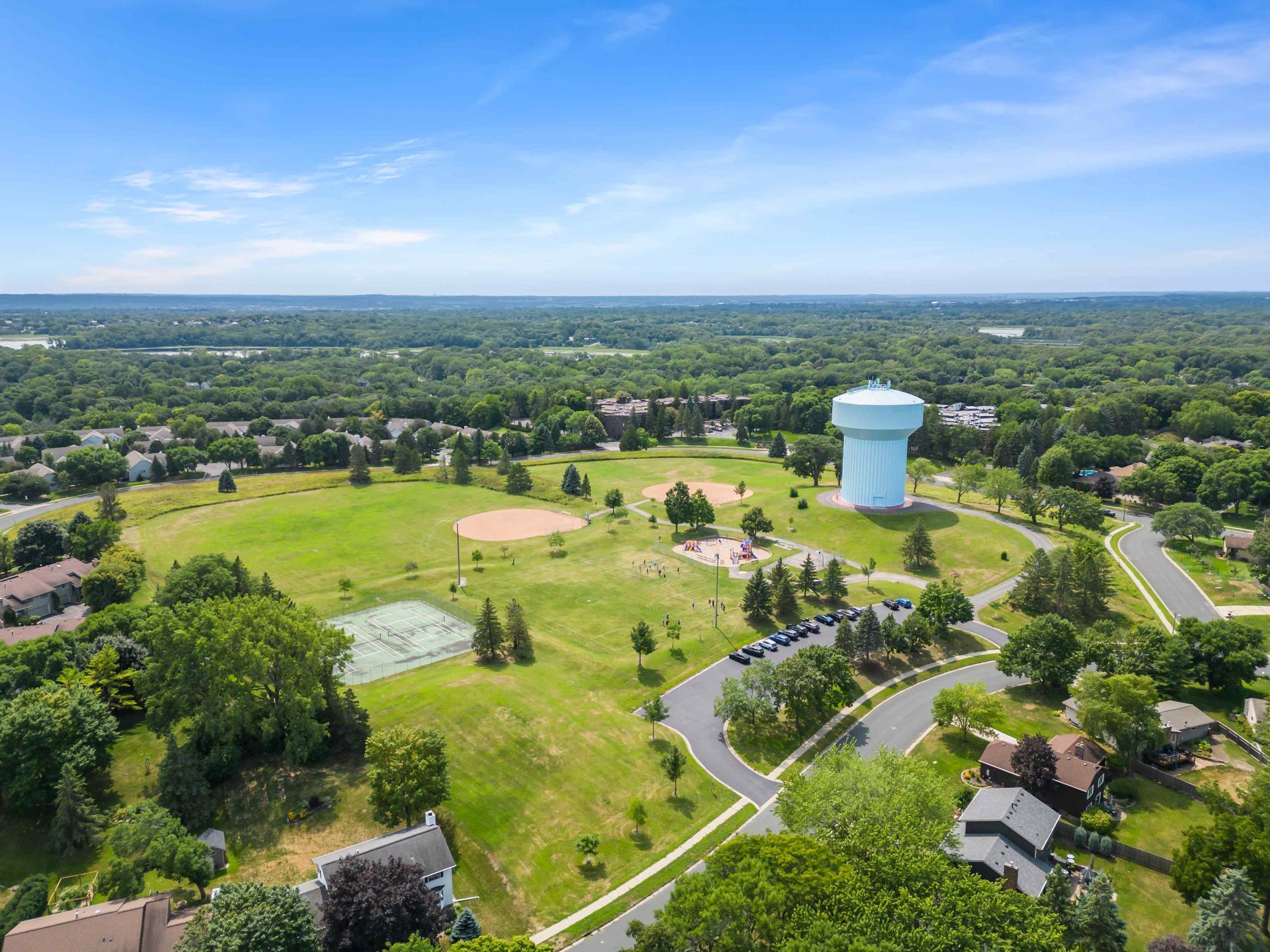 Aerial view of nearby recreational amenities featuring open green space, sports fields, tennis courts, playground facilities, and walking paths