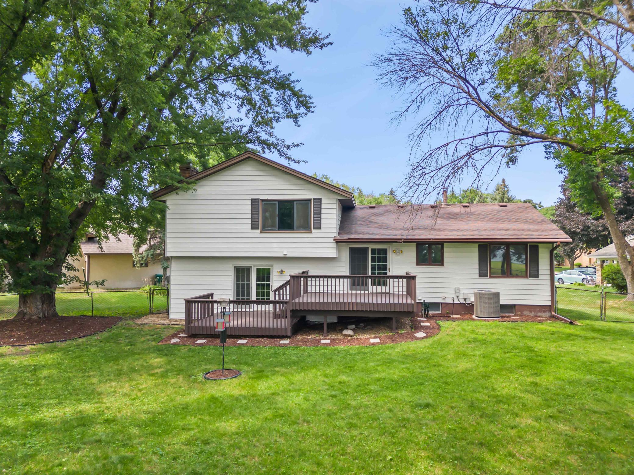 Spacious backyard with mature trees, lawn, fencing, and a raised deck for outdoor relaxation and entertaining