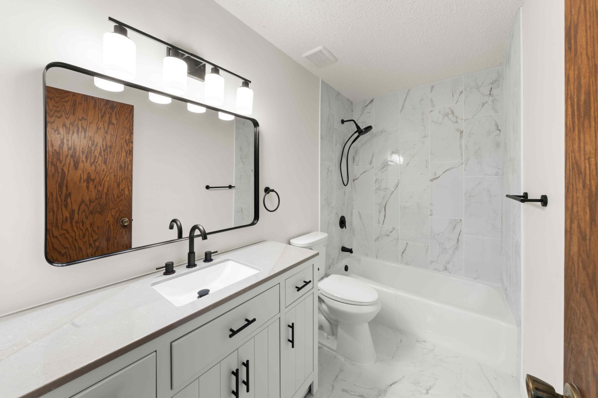 Updated full bath featuring a modern vanity, black fixtures, large mirror, and tiled flooring and shower surround