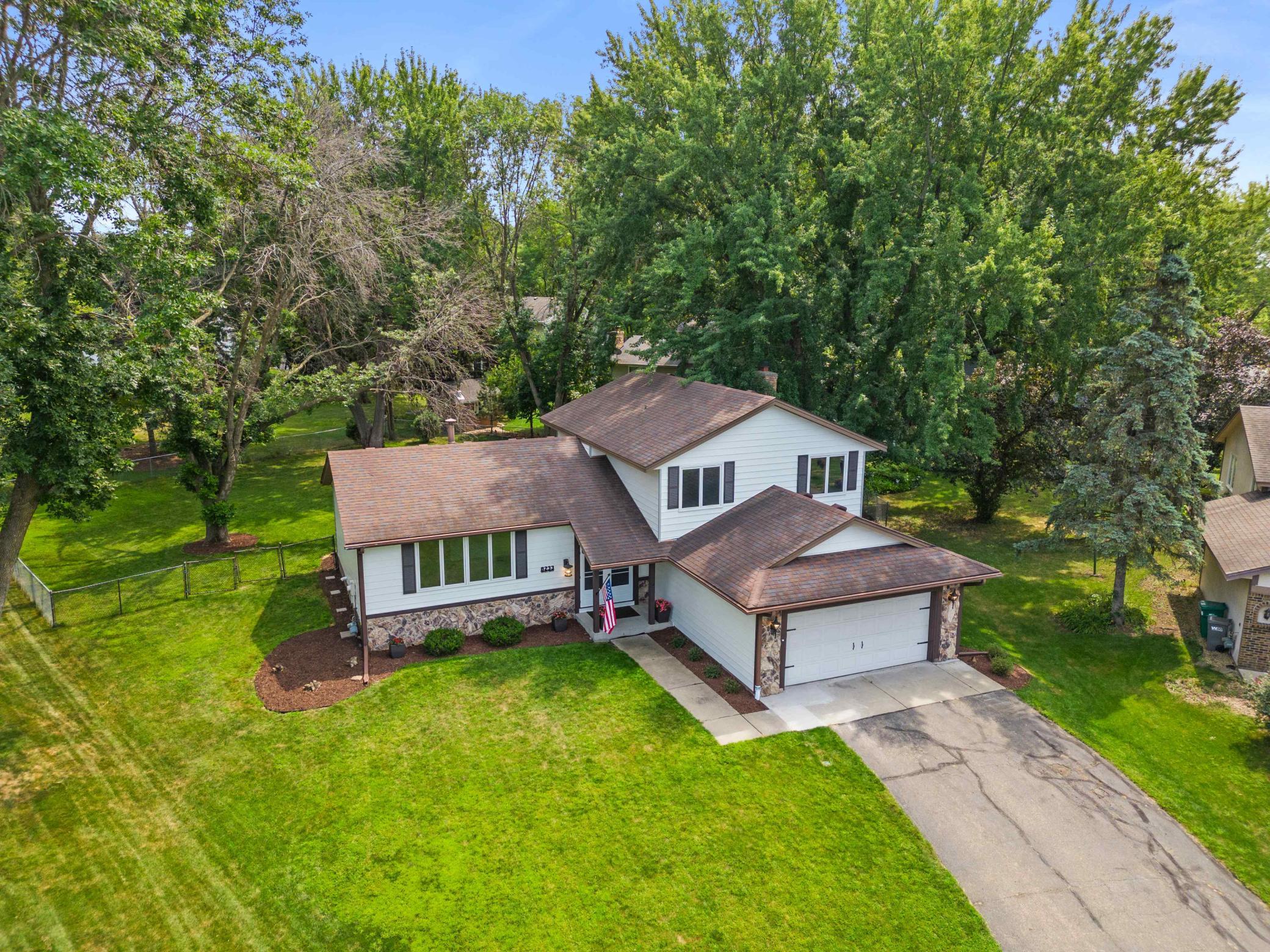 Elevated front view showcasing the home's multi-level design, attached two-car garage, mature landscaping, and tree-lined setting