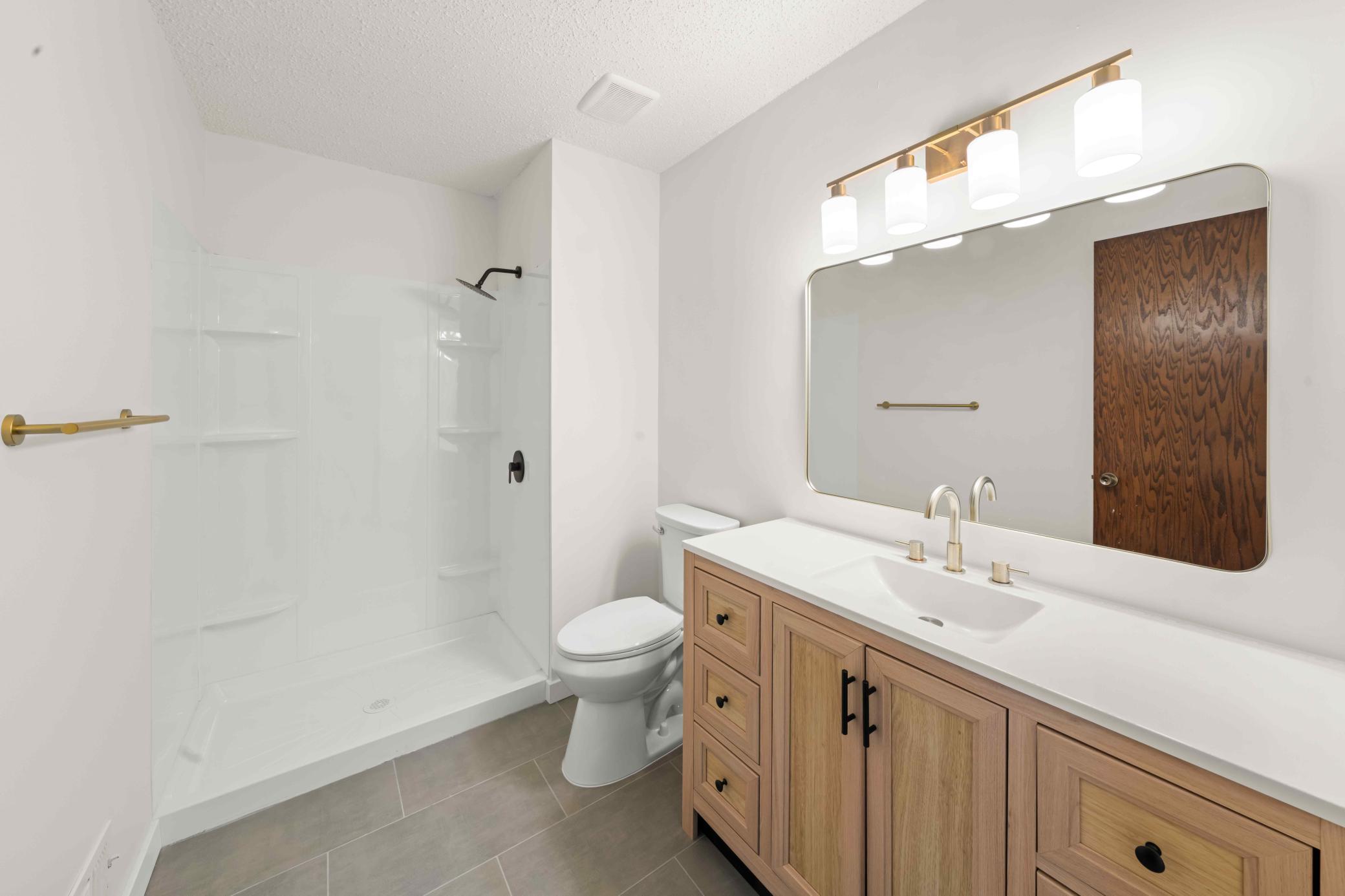 Updated private primary bath featuring a wood-tone vanity, quartz-style countertop, oversized mirror, modern fixtures, and walk-in shower