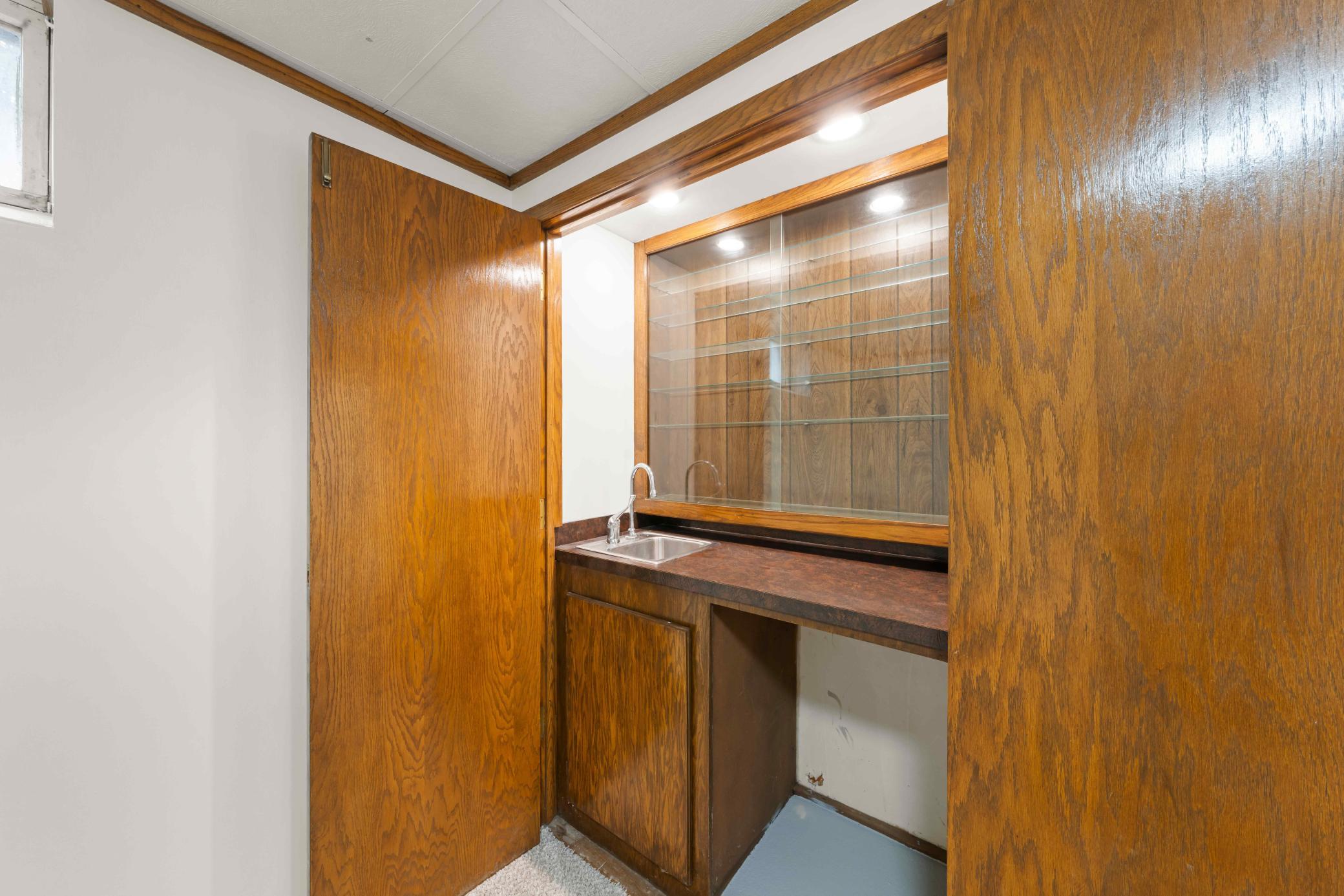 Built-in wet bar with sink, cabinetry, countertop workspace, glass shelving, and dedicated accent lighting