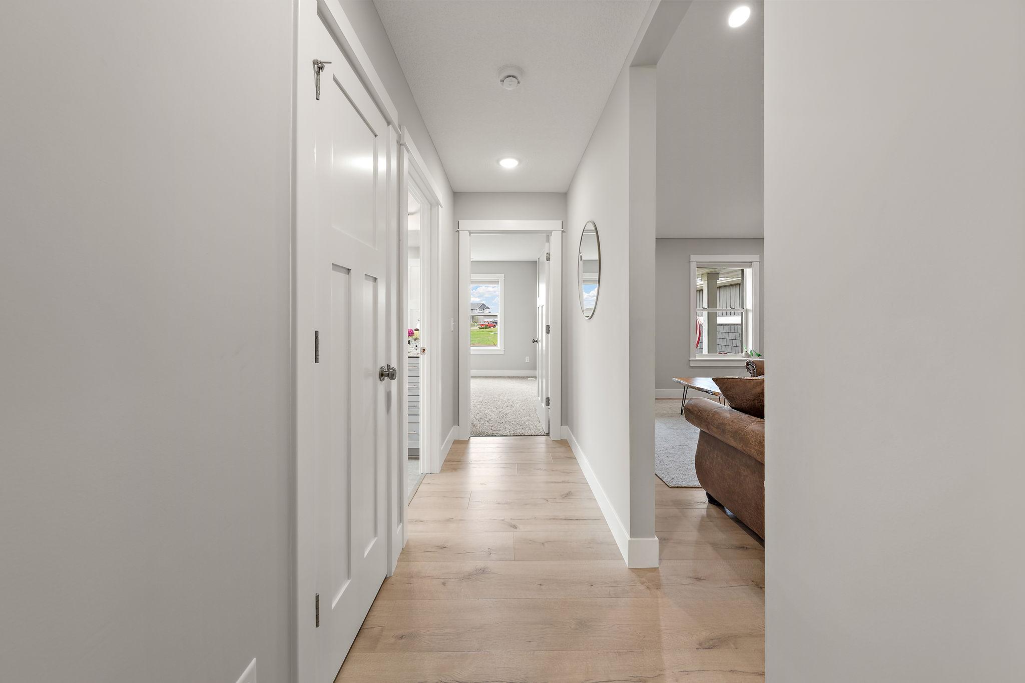 A view of the main floor hallway with living room on the right and the second bedroom directly ahead with carpeted floor. The hallway features a storage closet on the left and main floor bathroom on the left as well.