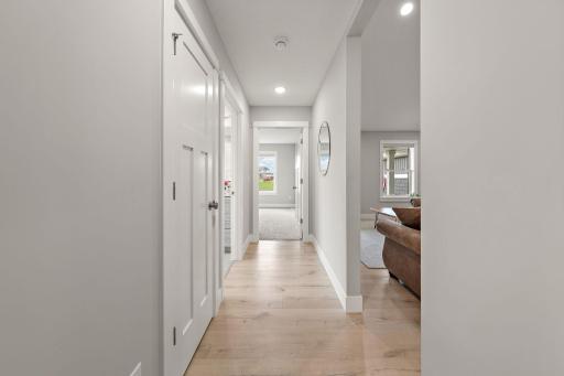 A view of the main floor hallway with living room on the right and the second bedroom directly ahead with carpeted floor. The hallway features a storage closet on the left and main floor bathroom on the left as well.