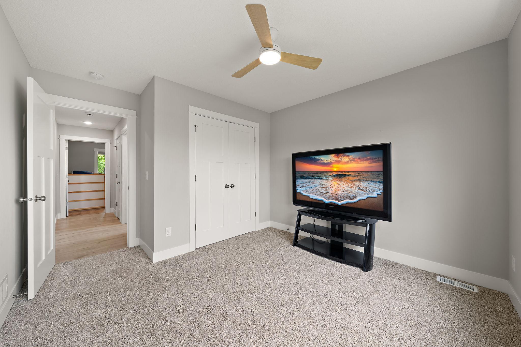 The second bedroom with open hallway door on the left with third bedroom visible across the hallway and clothes closets on the far right.