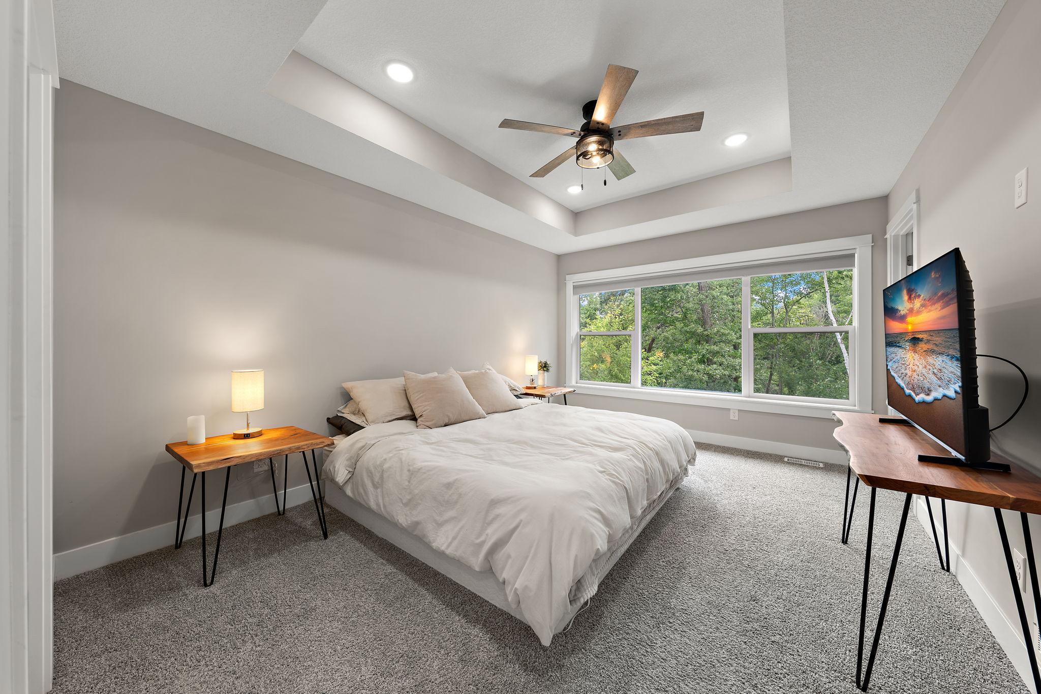 The primary bedroom features carpeting, a large window of the backyard and a ceiling fan.