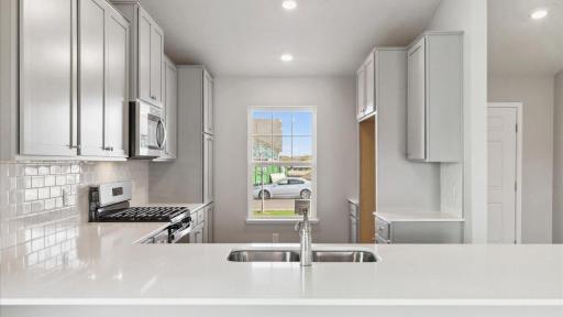 Gleaming quartz countertops with classic subway tile backsplash. Photo is of similar home. Colors and options may vary. Ask Sales Agent for details.