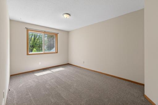 Second upper-level bedroom featuring updated carpeting, neutral finishes, and a large window with peaceful views.