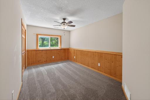 Lower-level bedroom with warm wood accents, updated carpeting, ceiling fan, and large closet for comfortable everyday living.
