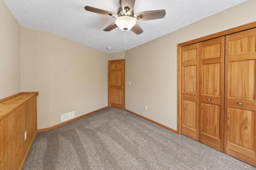 Spacious lower-level bedroom featuring rustic wood wainscoting, peaceful backyard views, and generous storage space.