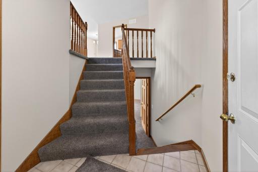 Welcoming split-entry foyer with oak railings, neutral finishes, and easy access to both upper and lower living spaces.