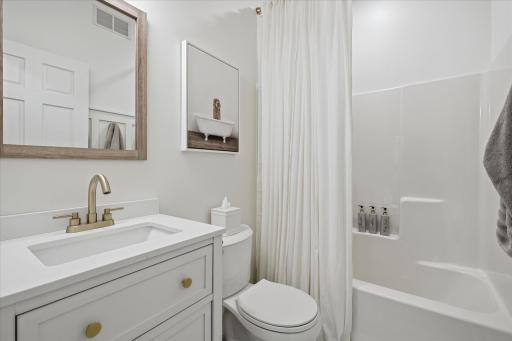 This hallway full bath features a quartz top vanity cabinet, a four shelf linen storage system, a wainscoting accent wall and a one-piece tub & shower surround. Tile flooring too!
