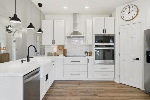 Whirlpool stainless steel appliances including a WiFi enabled wall oven. Solid surface countertops. A farm-style sink. A pantry closet. A tile backsplash. Black fixtures & pulls. Recessed lights & pendant lights. Wow. Just wow.