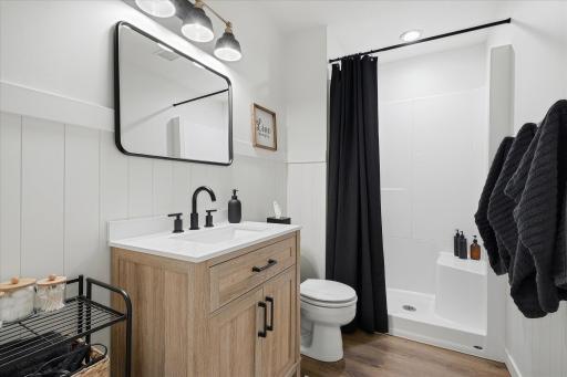 This 3/4 bath features a "Warm Rain" walk-in shower, LVP flooring, a vertical shiplap wall, a quartz-top vanity cabinet and modern black fixtures.