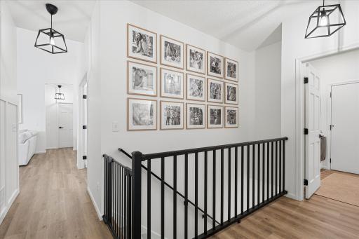 The hall just outside the private primary suite features an upgraded aluminum railing, beautiful flooring & lights, a board & batten accent wall and direct access to the laundry/mud room and attached garage.
