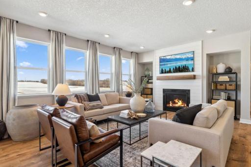 The family room is punctuated by a gas fireplace - which serves as a cozy bookend to the area and highlights a space that's flooded in natural light via these four soaring windows! Photo of a model home, color & options will vary.