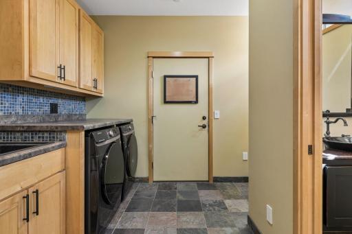 The mudroom includes the laundry area with a new washer and dryer, a deep work sink, a nook to hang coats, a coat closet, slate flooring, and maple built-in cabinets.
