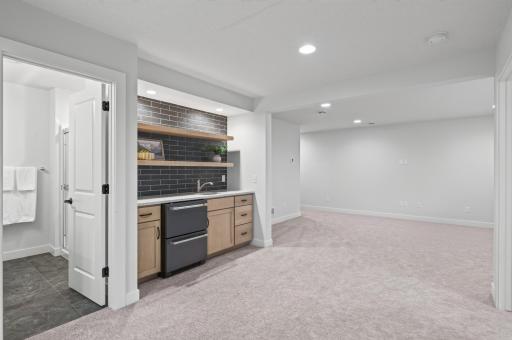 A standout wet bar featuring beautifully designed dark tile, floating shelves, a sink, and a fridge; ideal for refreshments after sport court play.