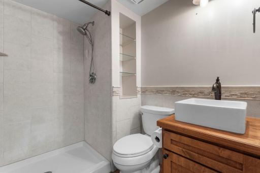 A third bathroom features a tiled walk-in shower, tiled flooring, vanity, and built-in shelving.