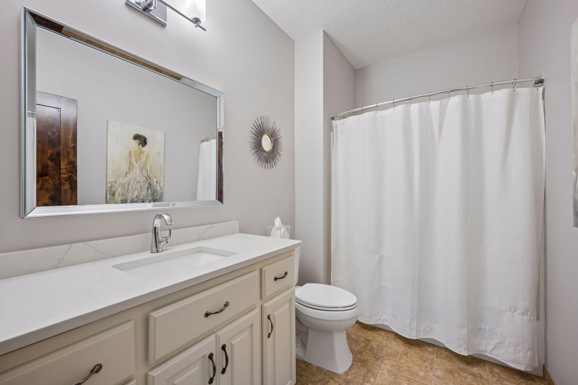 The main-level full bath features an extended vanity, a neutral color palette, and a tub/shower combination.