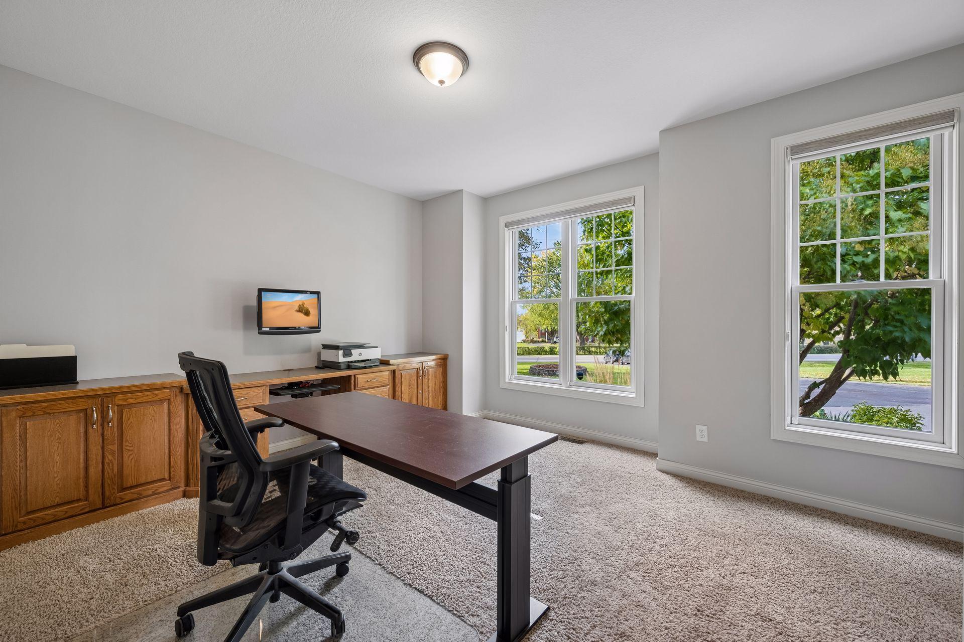 Two front-facing windows bring natural light into the second main-level bedroom, currently used as an office.