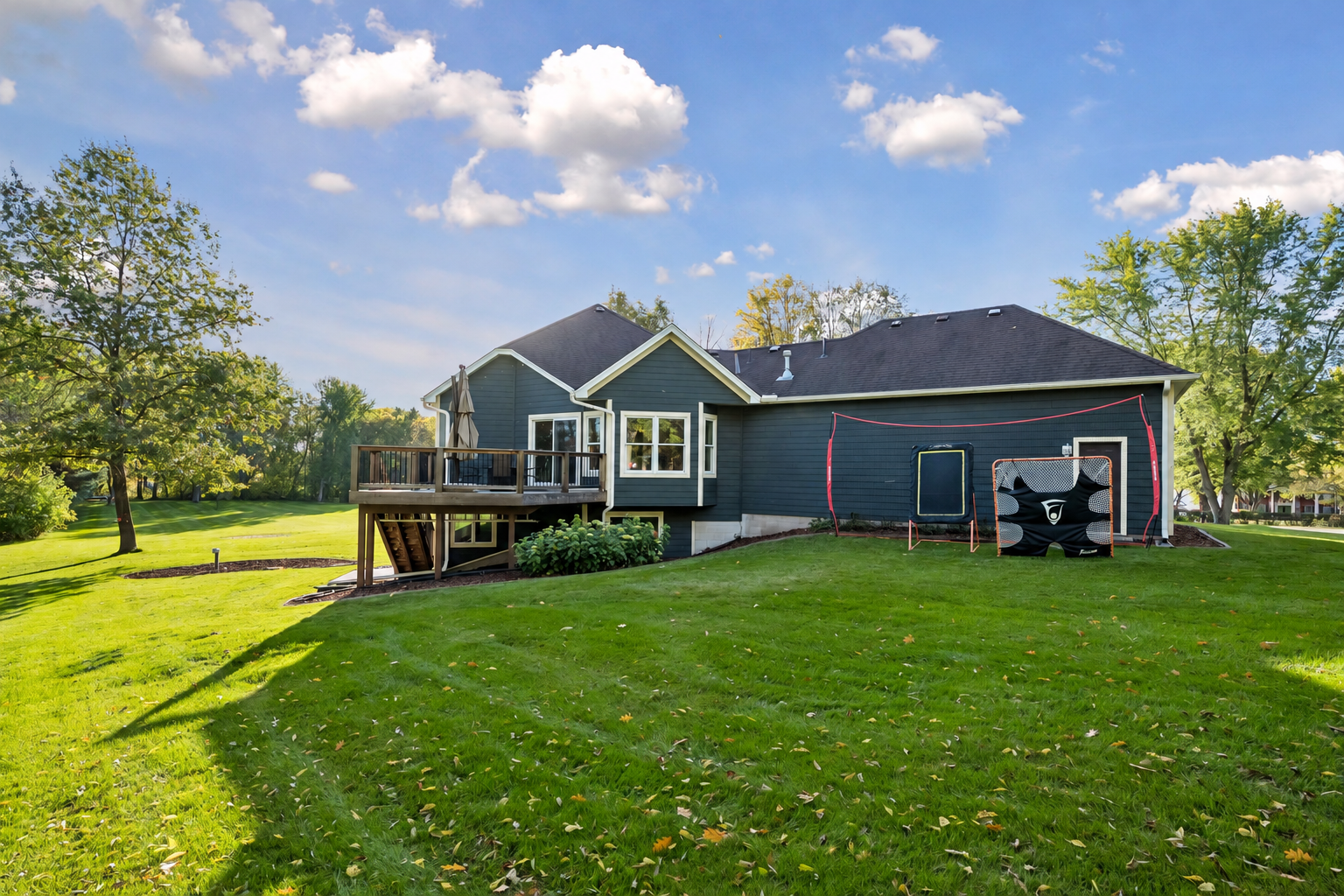 The rear view highlights the deck, mature trees, and expansive lawn surrounding the home.