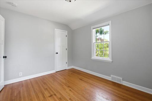Another bedroom offers warm hardwood flooring, neutral finishes, ample wall space, and a bright window overlooking the surrounding neighborhood.