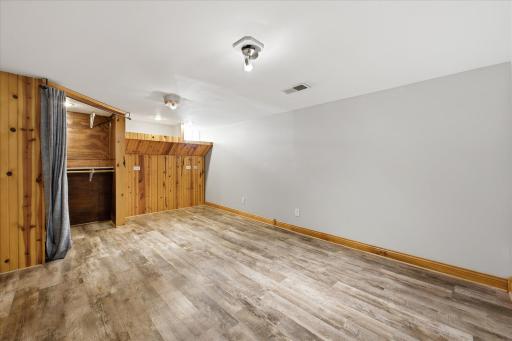 The finished lower-level room provides flexible living space with updated flooring, neutral walls, built-in shelving, and abundant wood paneling that adds warmth and character.