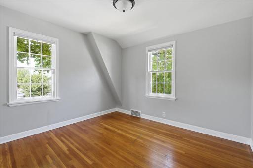 This spacious bedroom features beautiful hardwood floors, neutral walls, classic trim, and two windows that fill the room with natural light.
