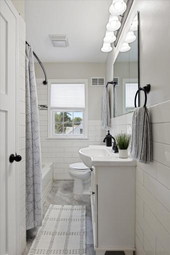 The updated full bathroom features crisp white tile, a modern vanity, a tub and shower combination, and a bright window that brings natural light into the space.