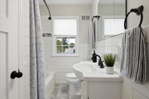 The updated full bathroom features crisp white tile, a modern vanity, a tub and shower combination, and a bright window that brings natural light into the space.