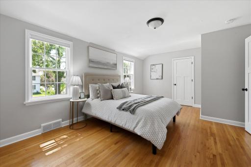 Natural light fills this comfortable bedroom through multiple windows, highlighting the hardwood floors, soft neutral finishes, and generous floor space for flexible furniture arrangements.