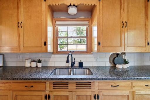A spacious kitchen work area features a double-basin sink beneath a window, generous granite counter space, extensive cabinetry, and a clean subway tile backsplash.