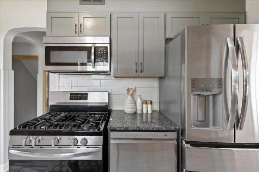 Stainless steel appliances, including a gas range, microwave, dishwasher, and French-door refrigerator, provide modern functionality while complementing the kitchen's classic cabinetry.
