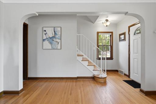 A welcoming foyer showcases the home's original character with hardwood floors, warm wood trim, an arched opening, and a charming staircase leading to the second floor.