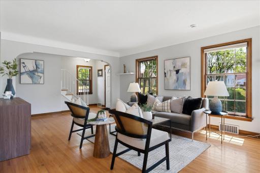 The bright living room features beautiful hardwood floors, generous windows, and classic wood trim, creating a comfortable gathering space filled with natural light and timeless character.