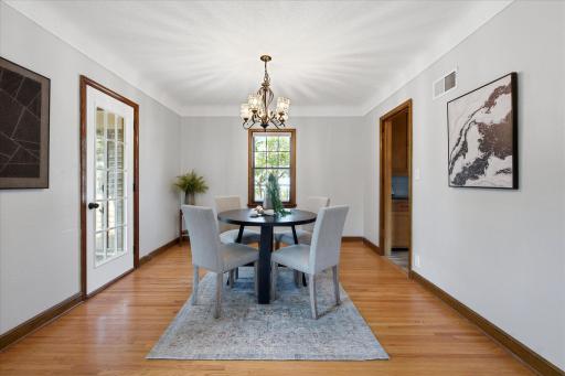 The dining room offers comfortable space for meals and gatherings, with hardwood floors, classic wood trim, a charming chandelier, and a bright window overlooking the neighborhood.