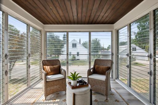 The inviting three-season porch offers a peaceful spot to relax, with walls of windows, comfortable seating, and a wood-paneled ceiling that adds warmth and character.