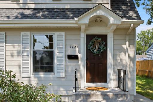 The front entry features an inviting covered portico, decorative columns, traditional shutters, and a warm wood door that adds timeless character and curb appeal.