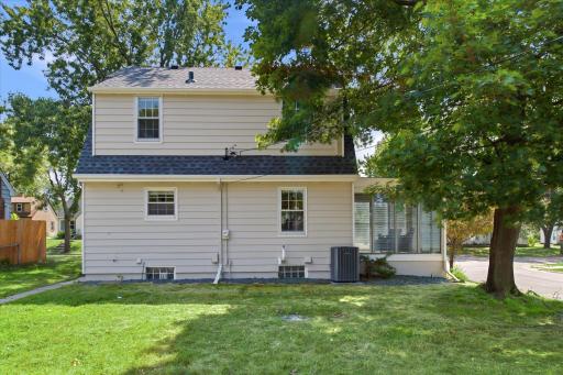 The rear exterior showcases the home's well-maintained siding, newer-looking mechanical equipment, mature trees, and a spacious grassy yard with convenient side access.