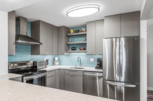 Updated kitchen featuring stainless steel appliances, gray cabinetry, open display shelving, and a light-filled layout.