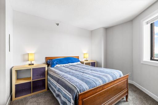 Guest bedroom featuring a warm wood bed frame, bedside lighting, neutral carpeting, and natural light.