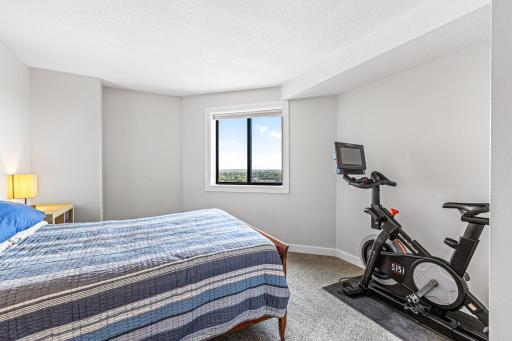 Spacious guest bedroom featuring neutral carpeting, room for exercise equipment, and a large window.