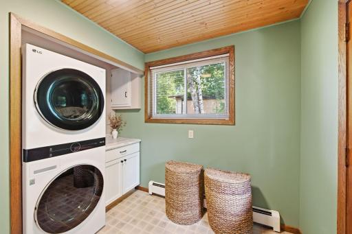 Dedicated laundry room with stacked washer and dryer, cabinetry, countertop workspace and window.