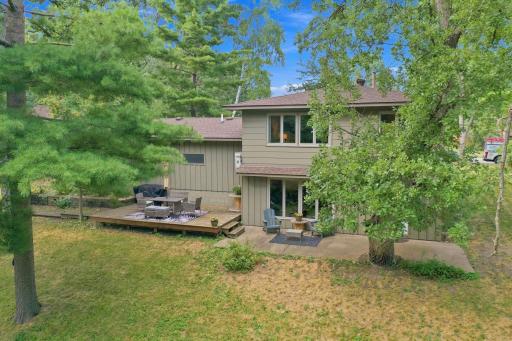 Rear aerial view showcasing the home, spacious deck and wooded backyard setting.