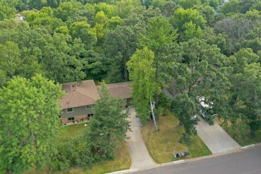 Front aerial view highlights the home tucked among mature trees with a concrete driveway.