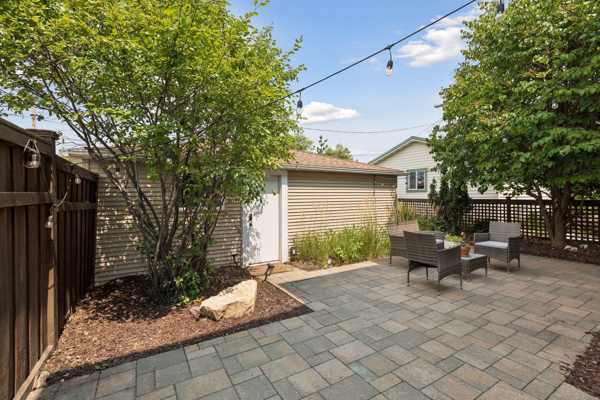 Stunning outdoor entertaining area with expansive paver patio, gardens, and privacy fence.