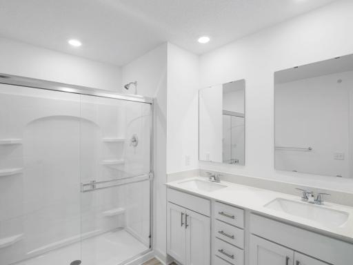 An elegant design in the bathroom showcases a large shower with framed glass enclosure and a chic vanity complete with dual sinks, ample cabinetry and a full wall-width mirror