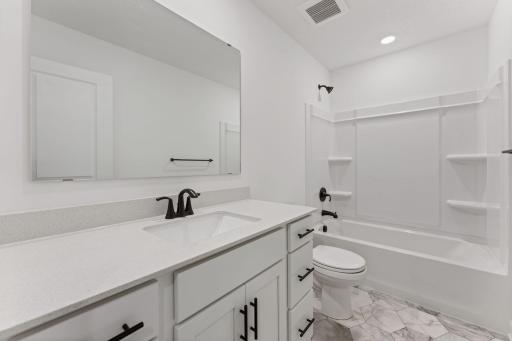 (Photo of a similar home, actual finishes may vary) Situated near the secondary bedrooms, this full-sized bathroom comes well-equipped with a quartz-topped vanity and a combination shower and tub to maximize the interior space.